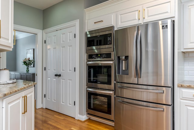 kitchen featuring white cabinetry, light hardwood / wood-style flooring, light stone counters, and appliances with stainless steel finishes