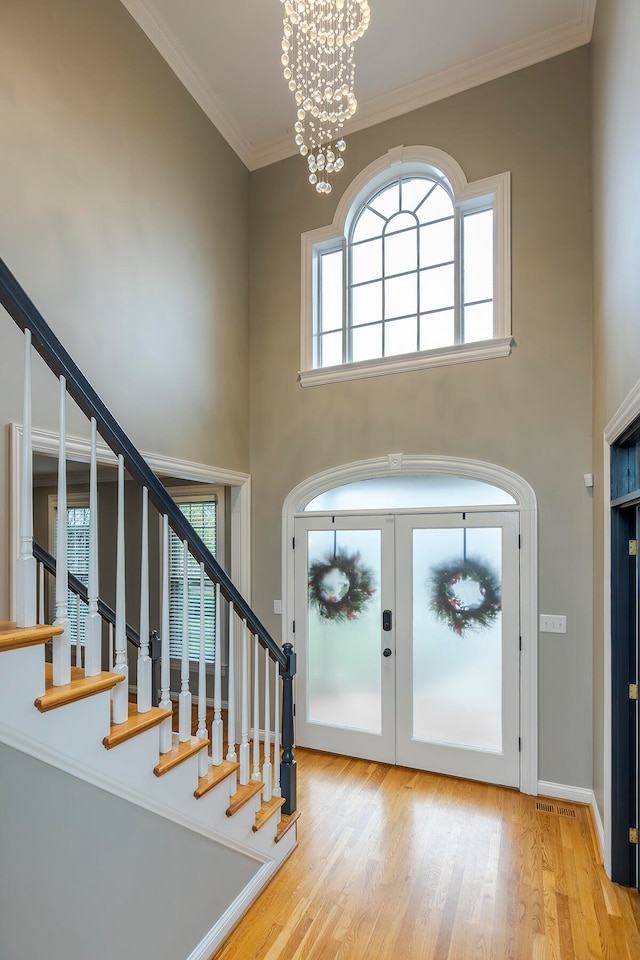 foyer entrance featuring a towering ceiling, light wood-type flooring, an inviting chandelier, and ornamental molding