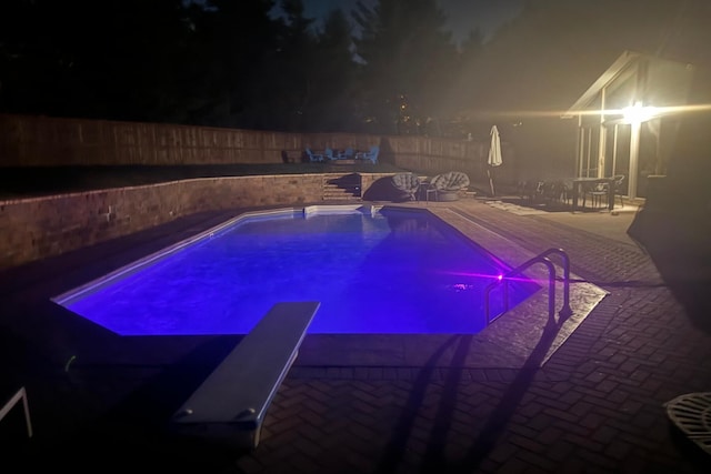 pool at twilight featuring a patio area and a diving board