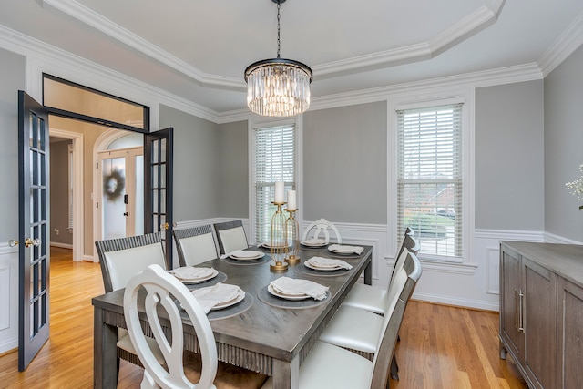 dining space with a raised ceiling, an inviting chandelier, ornamental molding, and light wood-type flooring