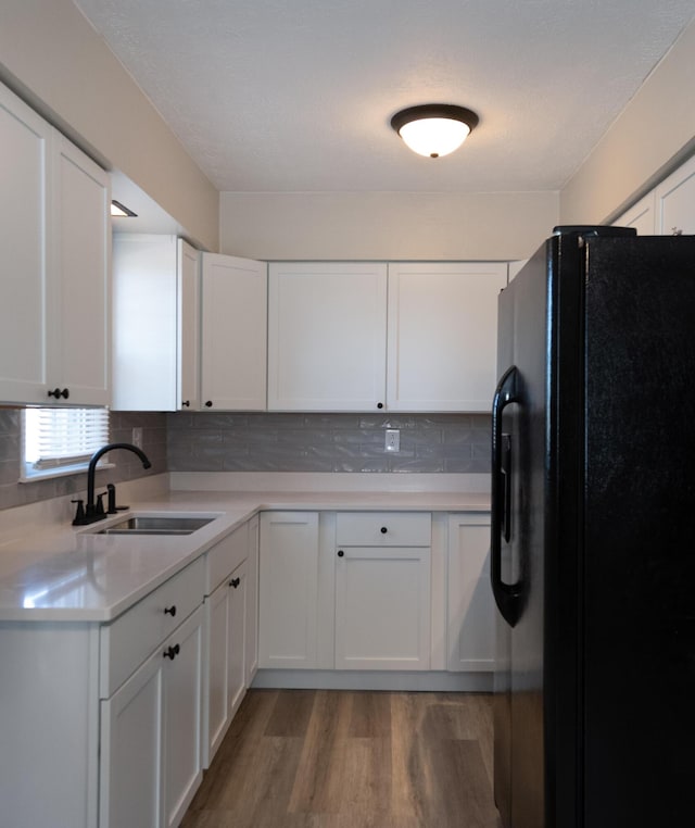 kitchen with light wood finished floors, tasteful backsplash, freestanding refrigerator, white cabinets, and a sink