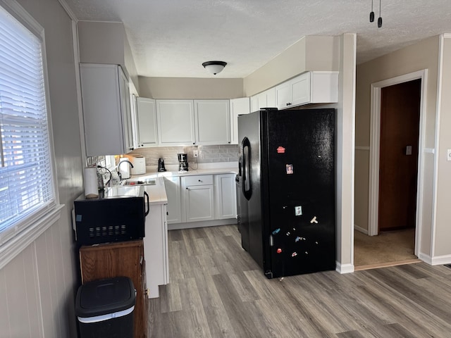 kitchen featuring backsplash, light wood-type flooring, light countertops, black fridge with ice dispenser, and a sink