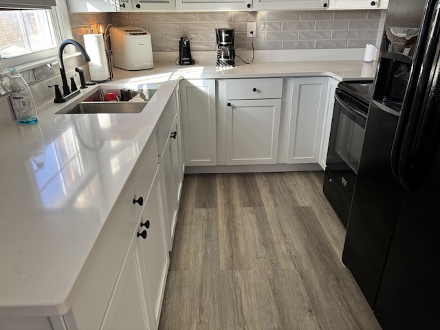 kitchen featuring wood finished floors, a sink, black appliances, white cabinetry, and tasteful backsplash