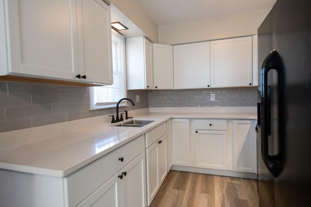 kitchen with light wood-type flooring, a sink, backsplash, white cabinetry, and freestanding refrigerator