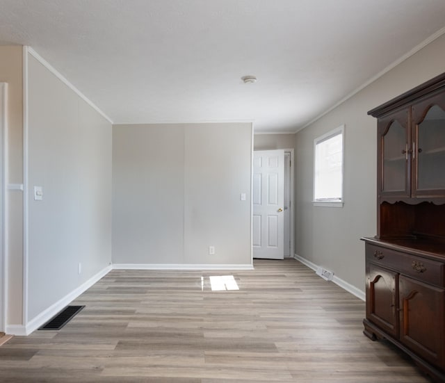 empty room with visible vents, baseboards, light wood-style floors, and crown molding