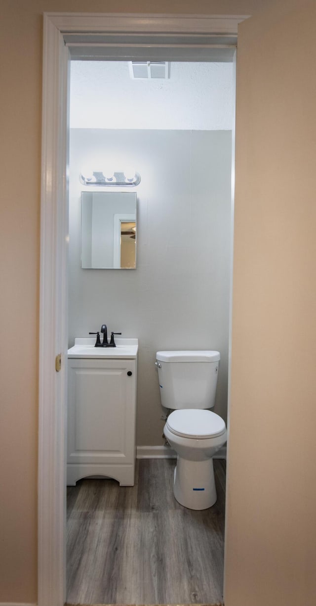 half bath with vanity, toilet, wood finished floors, and visible vents