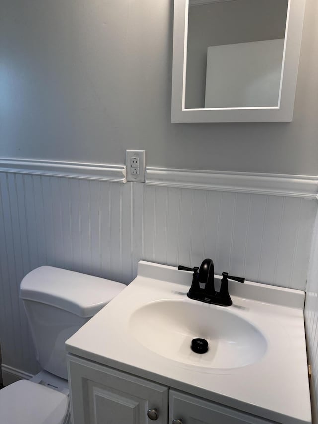 half bathroom with a wainscoted wall, toilet, and vanity