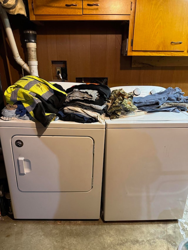 laundry room with washer and dryer, cabinets, and wood walls