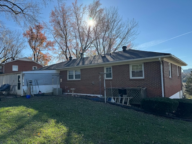 rear view of property with central AC unit and a lawn