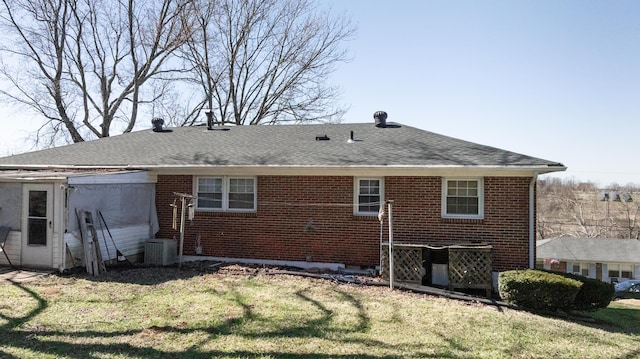 rear view of property with brick siding, central air condition unit, a shingled roof, and a yard