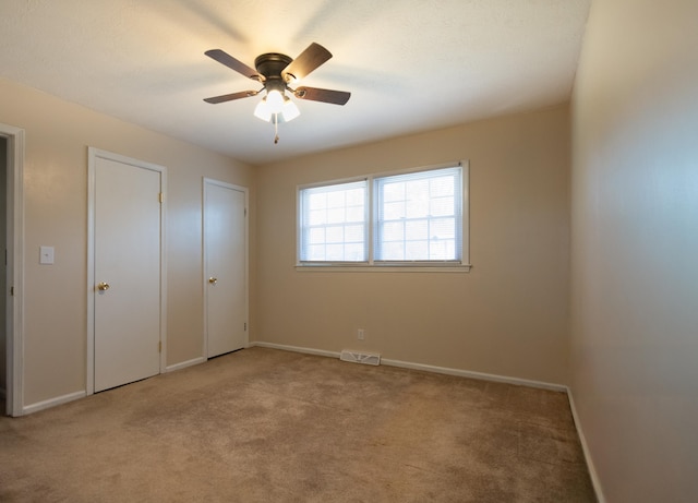 unfurnished bedroom featuring visible vents, ceiling fan, baseboards, multiple closets, and carpet flooring