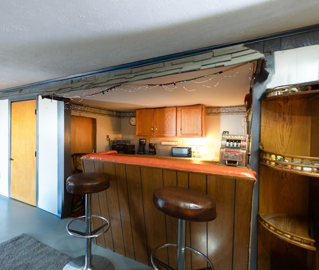 bar featuring a textured ceiling, a bar, concrete floors, and black microwave