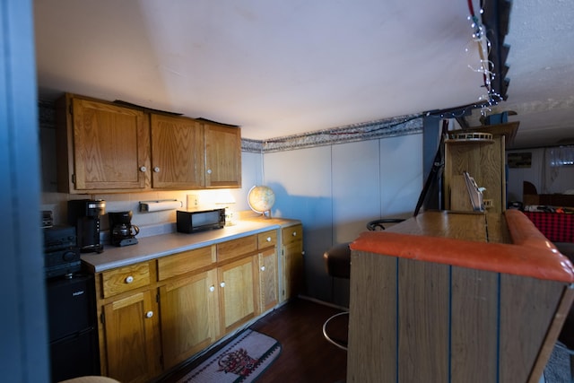 kitchen with dark wood-style floors, brown cabinetry, light countertops, and black microwave