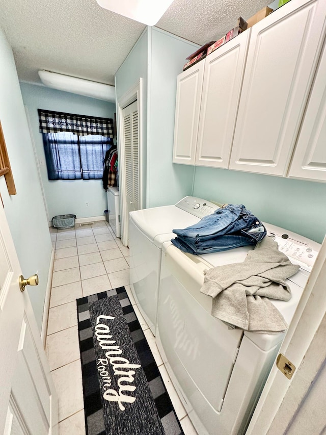 washroom with washer and dryer, light tile patterned flooring, cabinets, and a textured ceiling