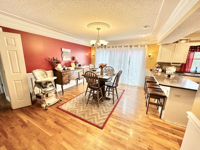 dining space with a chandelier, a textured ceiling, light hardwood / wood-style flooring, and crown molding