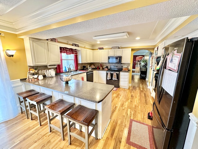 kitchen with kitchen peninsula, light wood-type flooring, ornamental molding, a breakfast bar, and black appliances