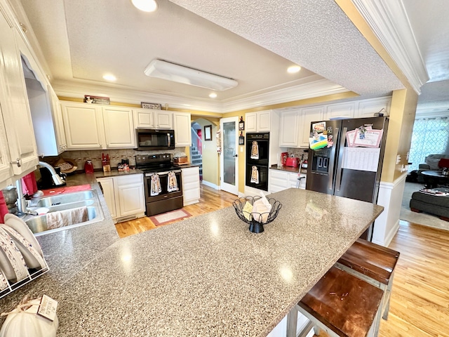 kitchen with white cabinets, light wood-type flooring, a tray ceiling, and black appliances