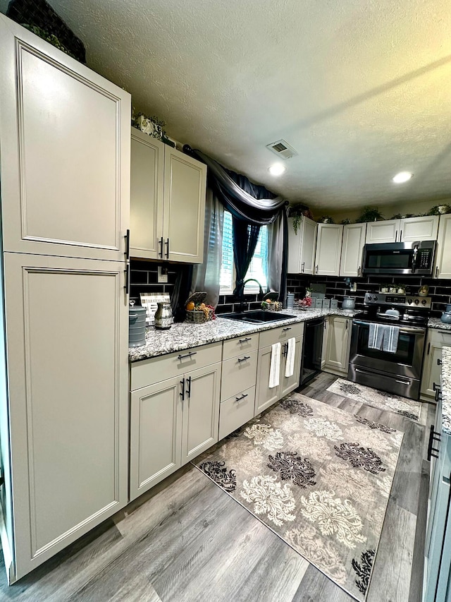 kitchen featuring light stone countertops, light wood-type flooring, sink, and appliances with stainless steel finishes