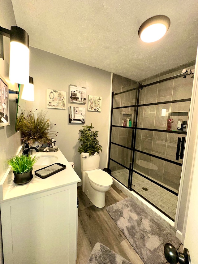 bathroom featuring tiled shower, toilet, wood-type flooring, and a textured ceiling