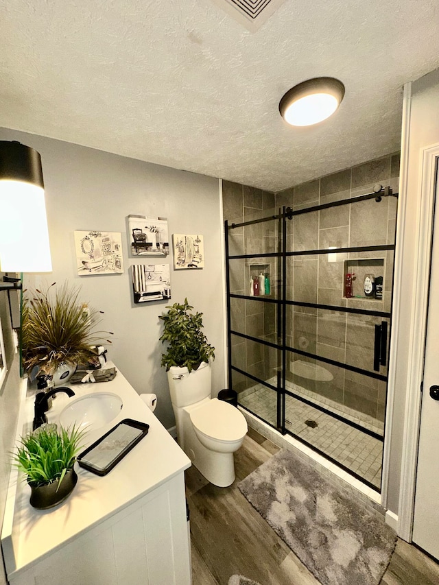 bathroom featuring a tile shower, vanity, wood-type flooring, and a textured ceiling