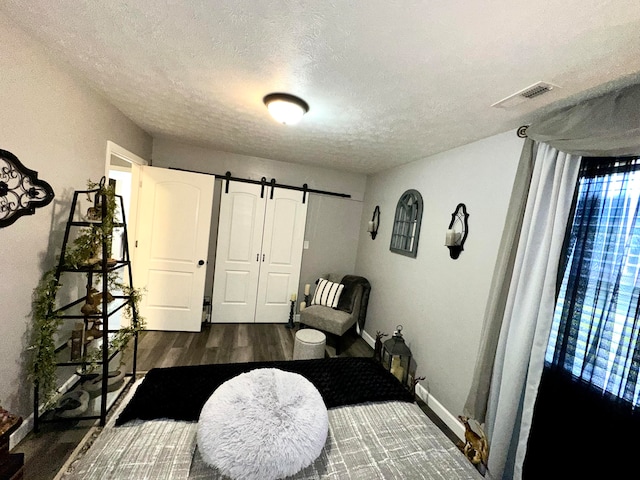 bedroom with a textured ceiling, a barn door, and dark wood-type flooring