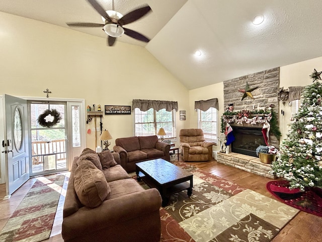 living room featuring ceiling fan, a textured ceiling, lofted ceiling, a fireplace, and hardwood / wood-style flooring