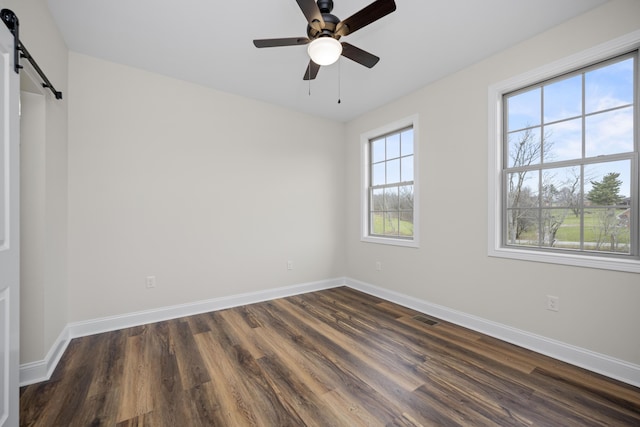 spare room featuring a barn door, ceiling fan, and dark wood-type flooring