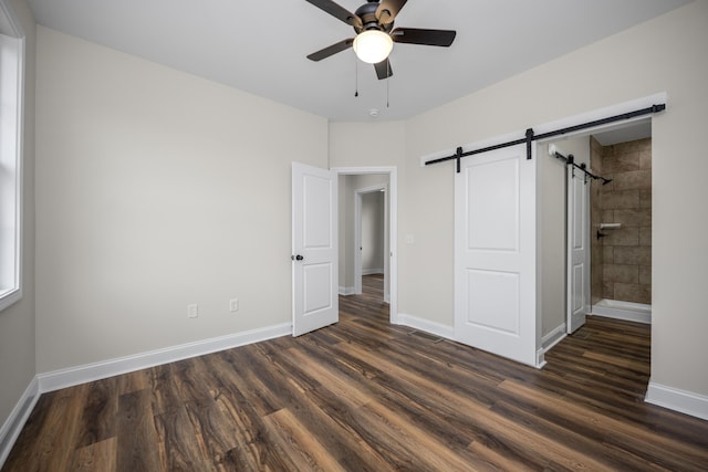 unfurnished bedroom featuring a barn door, ceiling fan, dark hardwood / wood-style flooring, and ensuite bath