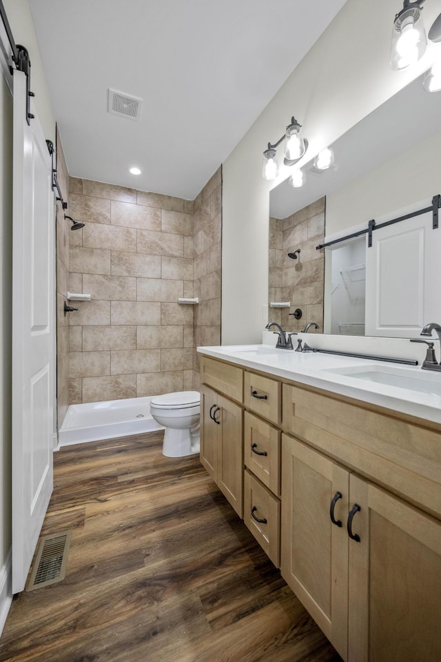 bathroom with a tile shower, vanity, hardwood / wood-style flooring, and toilet