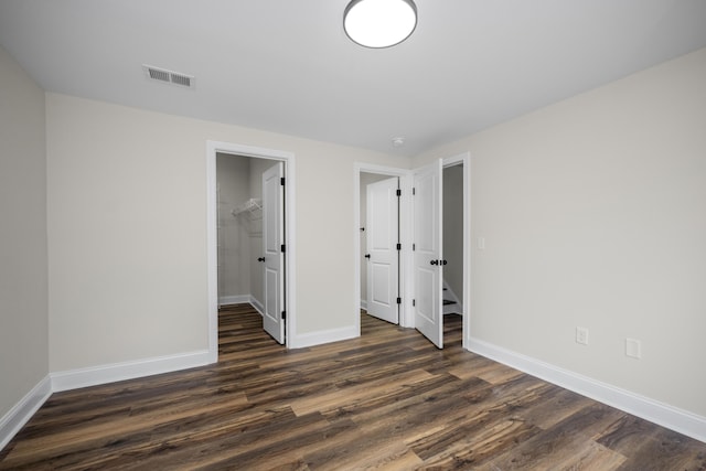 unfurnished bedroom with a walk in closet, a closet, and dark wood-type flooring