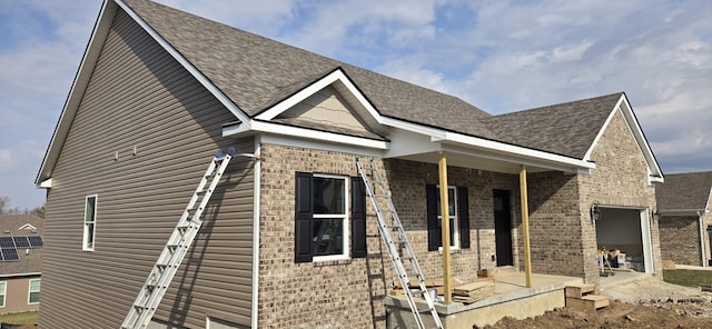 exterior space with brick siding, a patio area, a garage, and roof with shingles