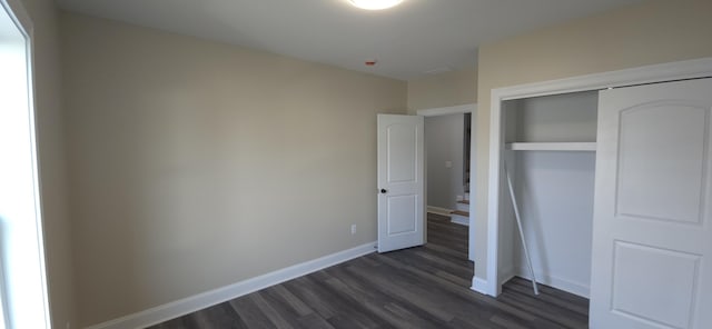 unfurnished bedroom featuring dark wood finished floors, a closet, and baseboards