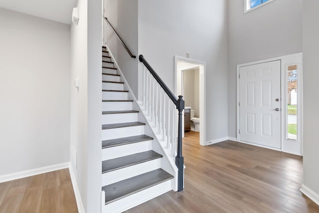 foyer entrance with a high ceiling, stairs, baseboards, and wood finished floors