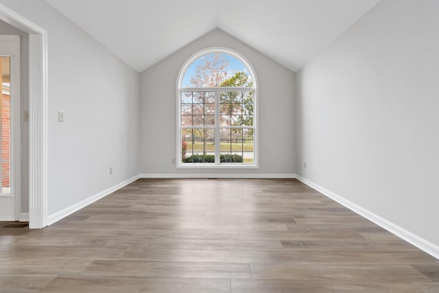 empty room featuring lofted ceiling, plenty of natural light, baseboards, and wood finished floors