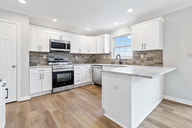 kitchen featuring stainless steel appliances, a peninsula, a sink, white cabinets, and light wood-type flooring