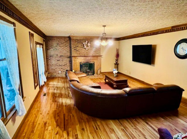 living room with a fireplace, an inviting chandelier, ornamental molding, and hardwood / wood-style flooring