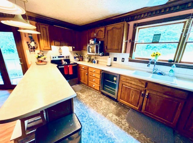 kitchen with pendant lighting, sink, a textured ceiling, appliances with stainless steel finishes, and beverage cooler