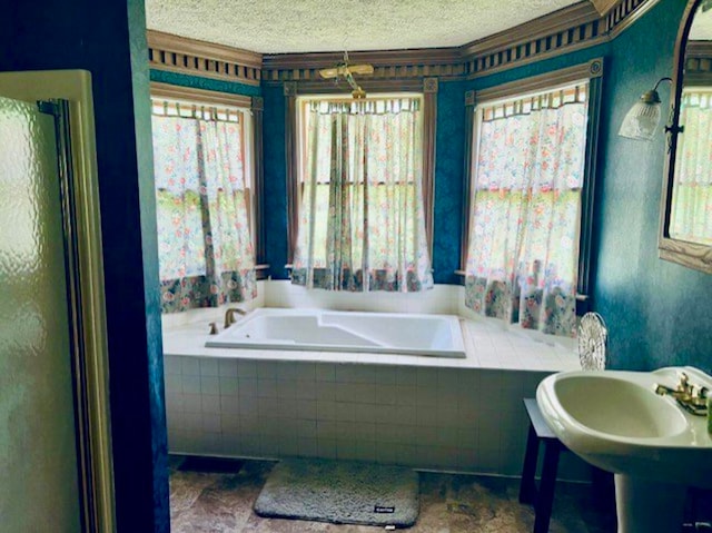 bathroom featuring tiled tub, a healthy amount of sunlight, and a textured ceiling