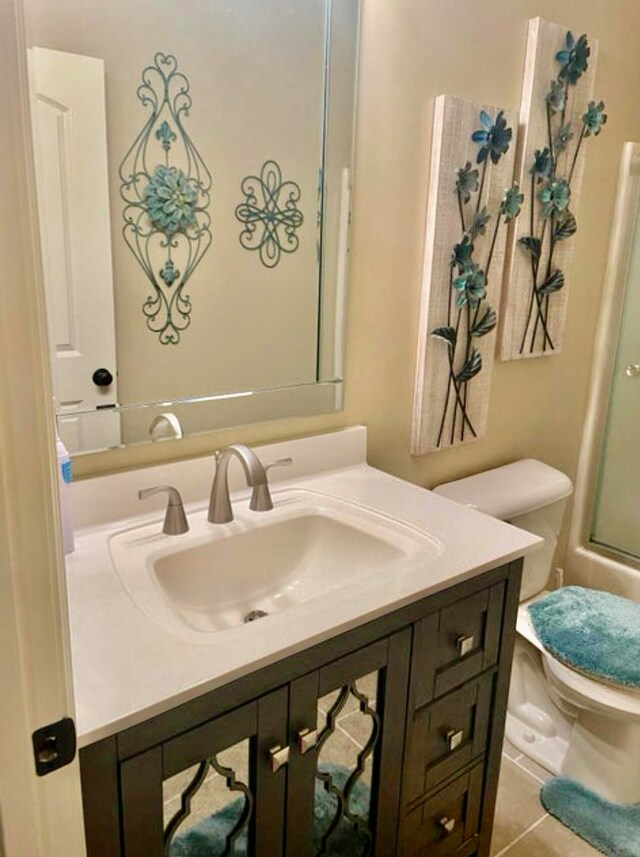 bathroom featuring tile patterned flooring, vanity, a shower with shower door, and toilet