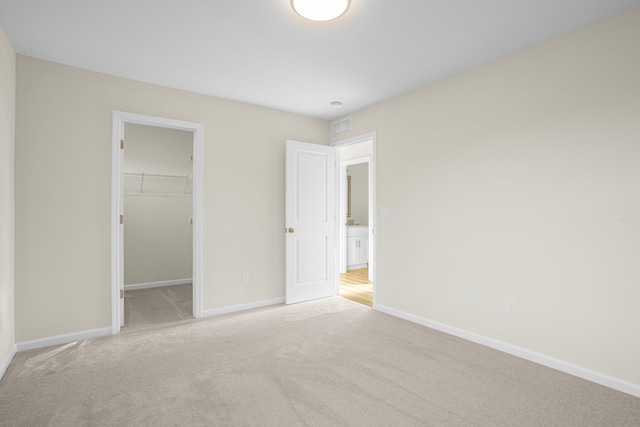 unfurnished bedroom with a walk in closet, light colored carpet, and a closet