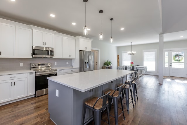 kitchen with appliances with stainless steel finishes, dark hardwood / wood-style flooring, white cabinetry, and a kitchen island