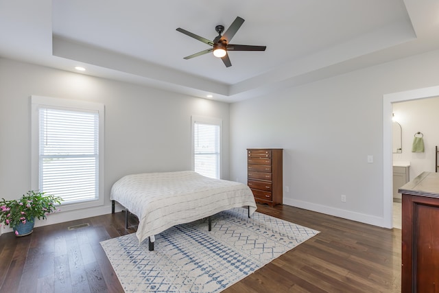 bedroom featuring a raised ceiling, ensuite bathroom, ceiling fan, and dark hardwood / wood-style floors