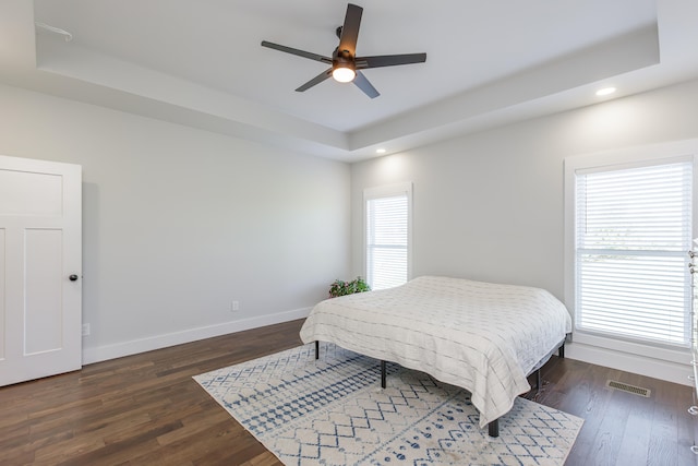 bedroom featuring dark hardwood / wood-style floors, ceiling fan, and a tray ceiling