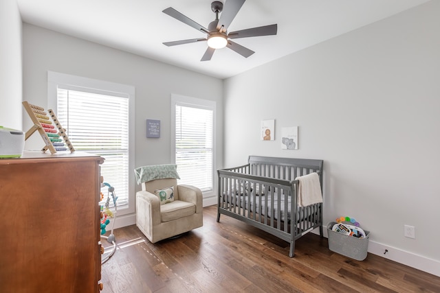 bedroom featuring multiple windows, a nursery area, dark wood-type flooring, and ceiling fan