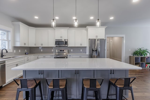 kitchen with hanging light fixtures, sink, appliances with stainless steel finishes, a kitchen island, and white cabinetry