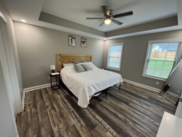 bedroom with ceiling fan, dark hardwood / wood-style floors, and a tray ceiling