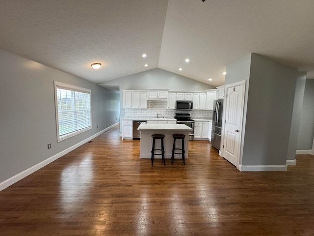 kitchen featuring dark wood-type flooring, white cabinets, appliances with stainless steel finishes, a kitchen island, and a breakfast bar area