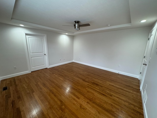 empty room with a raised ceiling, ceiling fan, and dark hardwood / wood-style flooring