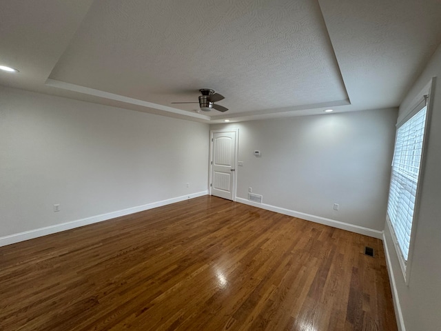 unfurnished room featuring a tray ceiling, ceiling fan, dark wood-type flooring, and a textured ceiling