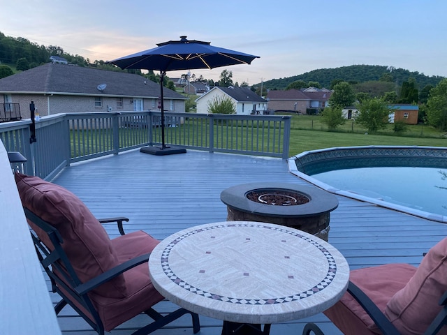 pool at dusk with a lawn, a wooden deck, and a fire pit